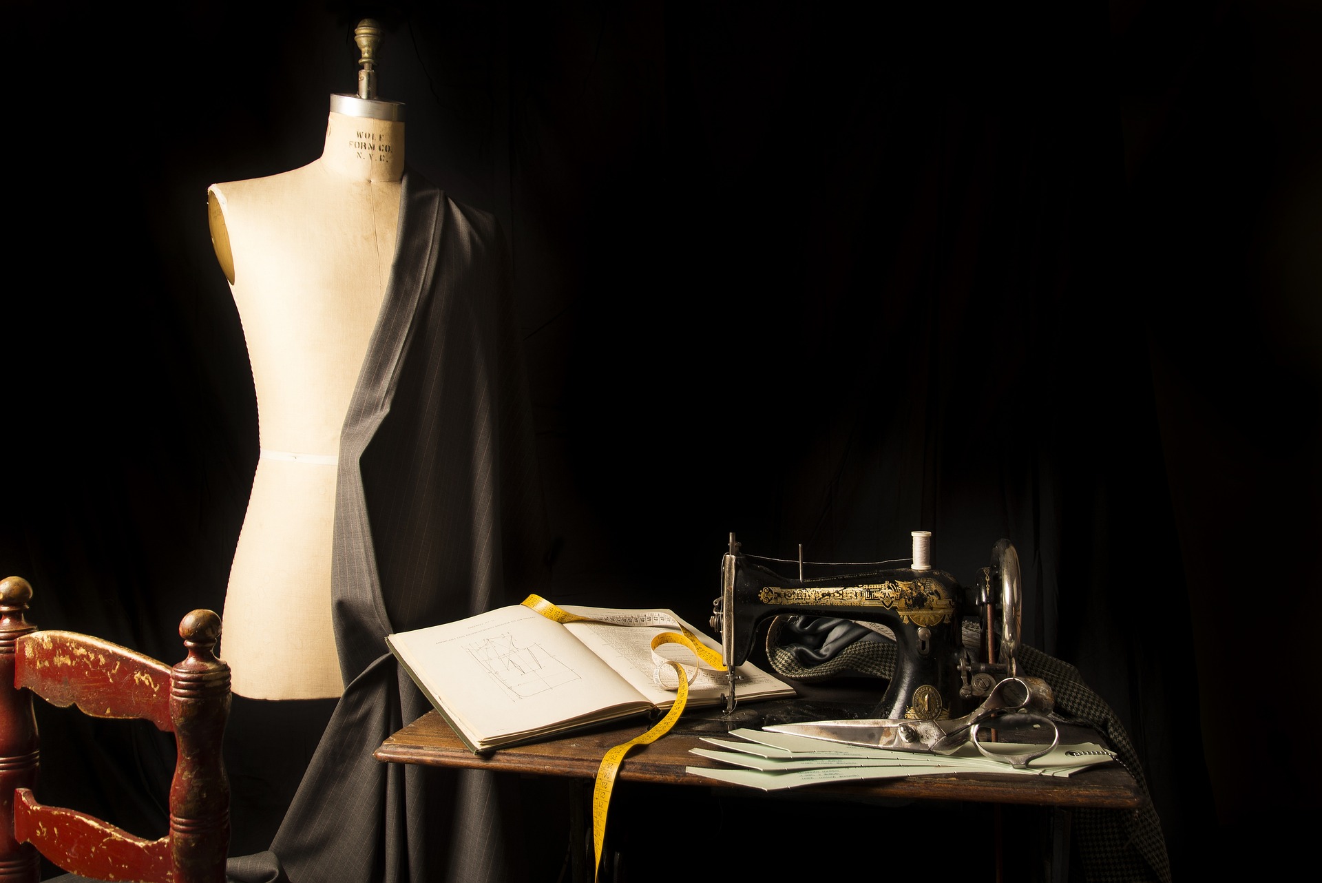 Vintage sewing machine and an open book on a table in front of a dress form and black background